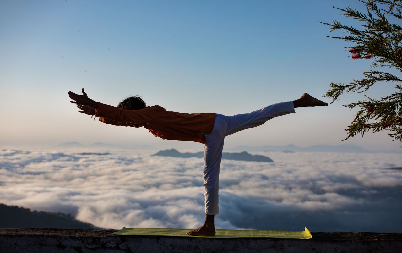 Mastering the First Impression: Your intriguing post title goes here Person practicing yoga in warrior pose above a scenic cloudscape during sunrise.
