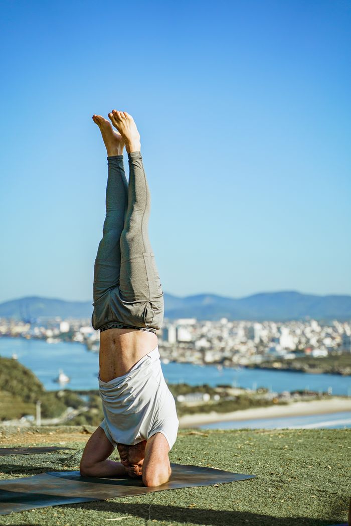amenities Man performing a headstand yoga pose outdoors on a sunny day with city skyline.