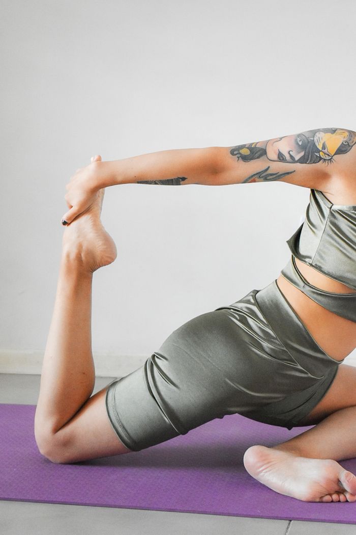 our-story Female athlete in sportswear practicing a stretching pose on a yoga mat.